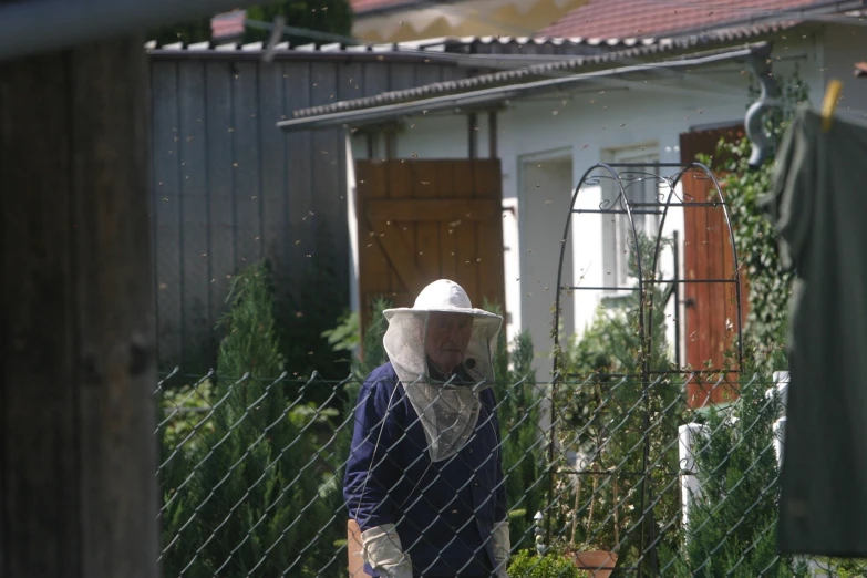 a man wearing a hat standing next to a fence, a photo, hive, eastern european, shot from a distance, veil