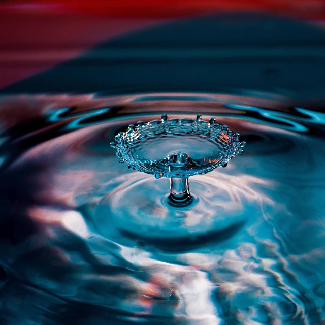 a close up of a water drop with a red background, art photography, floating crown, water flowing through the sewer, reflections on a glass table, blue water