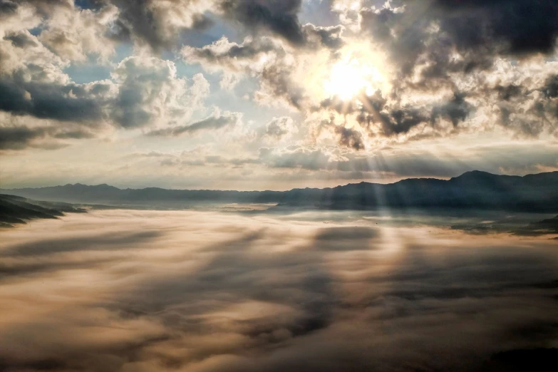 the sun shines through the clouds above the mountains, a tilt shift photo, by Tadashige Ono, blanket of fog, wide high angle view, beautifull puffy clouds. anime, beams of light from sky