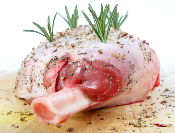 a piece of meat sitting on top of a wooden cutting board, by Samuel Scott, shutterstock, renaissance, human lamb hybrid, white muzzle and underside, herb, stock photo