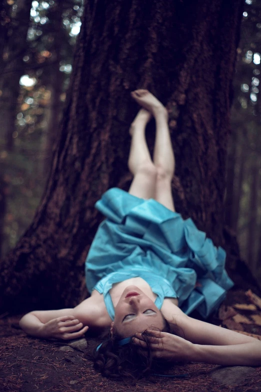 a woman laying on the ground in front of a tree, a portrait, inspired by Brooke Shaden, icey blue dress, looking up, retro photography, forest style studio shot