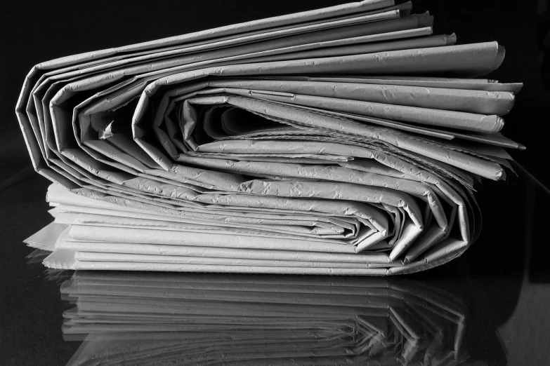 a stack of newspapers sitting on top of a table, a picture, by John Murdoch, private press, abstract photography, folds, reflection, black & white