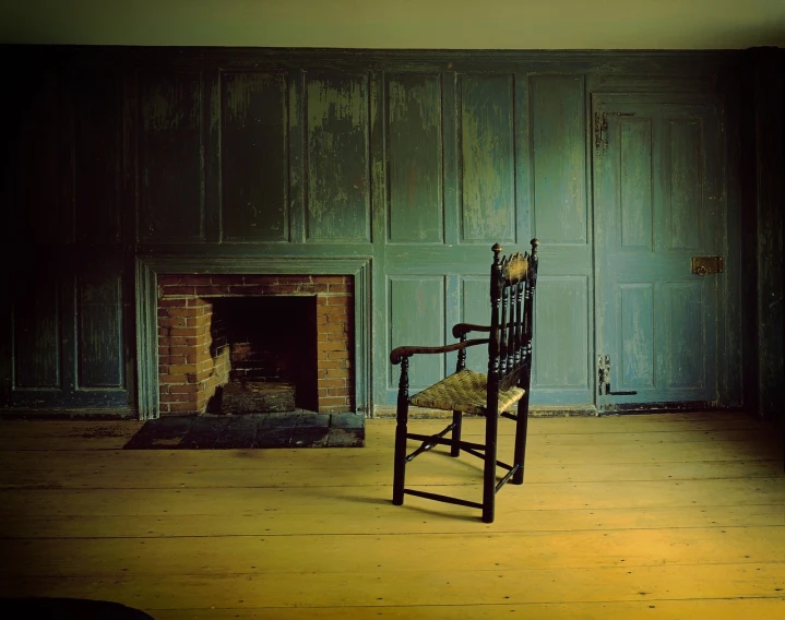 a chair sitting in front of a fireplace in a room, by Robert Brackman, distressed paint, old wood floors, mystic, peter