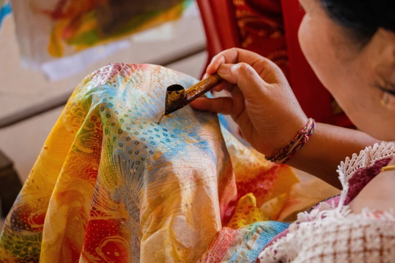 a woman cutting a piece of fabric with a pair of chopsticks, a detailed painting, by Pacita Abad, pixabay, process art, flowing golden scarf, festival of rich colors, hand painted textures on model, diaphanous iridescent cloth