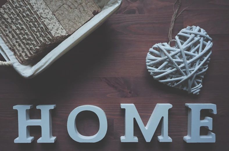 a piece of bread sitting on top of a wooden table, a picture, folk art, letters, homeloaf, banner, my home