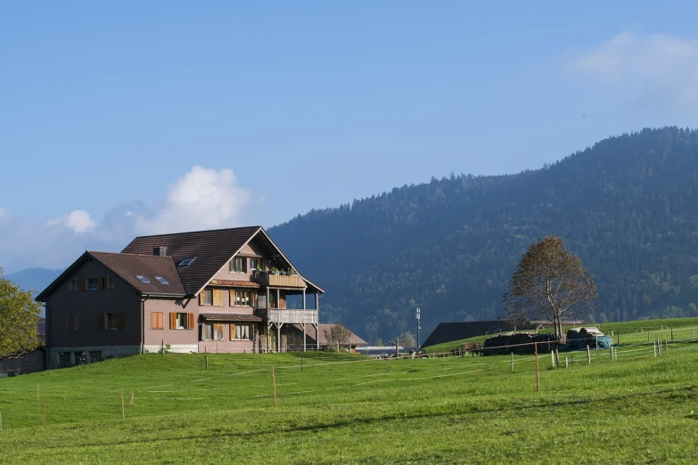 a house sitting on top of a lush green hillside, a picture, by Thomas Häfner, shutterstock, mountain behind meadow, herzog de meuron, view from the street, late morning