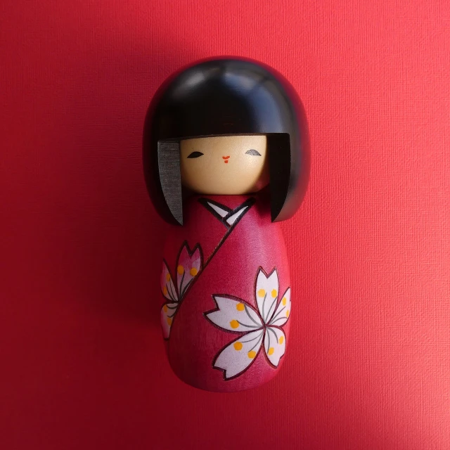 a close up of a doll on a red wall, a picture, inspired by Takehisa Yumeji, flickr, mingei, sakura flower, cute funny figurine wooden, hand painted, amy sol in the style of