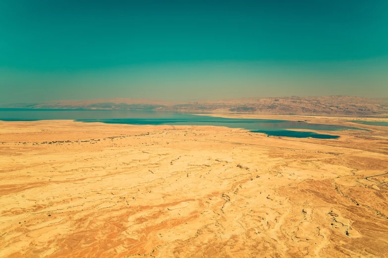 a large body of water sitting in the middle of a desert, a tilt shift photo, israel, retro stylised, aerial iridecent veins, amazing landscape in background