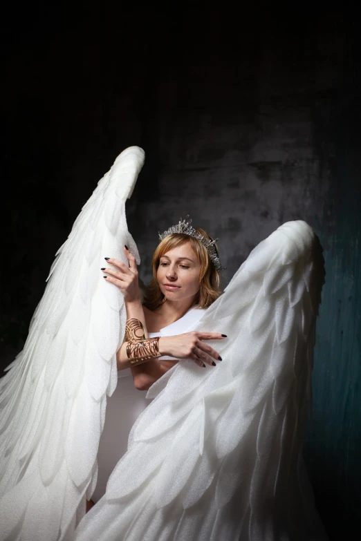 a woman in a wedding dress holding an angel's wings, inspired by Marie Angel, baroque, cosplay photo, in a dark studio room, with two pairs of wings, pose 1 of 1 6