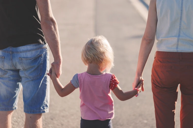 a group of people walking down a street holding hands, a picture, by Brad Holland, pexels, incoherents, portrait of family of three, tiny girl looking on, shaded, hand holding cap brim