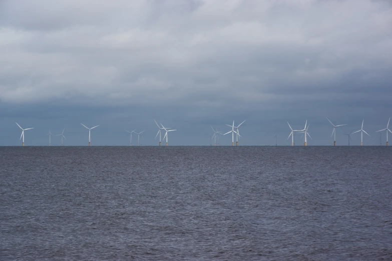 a large body of water with wind turbines in the background, purism, overcast weather, trident, celebration, in formation