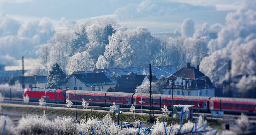 a large long train on a steel track, by Werner Gutzeit, flickr, with red berries and icicles, small town surrounding, cold as ice! 🧊, red roofs