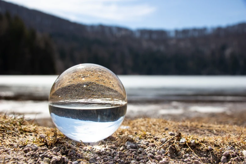 a glass ball sitting on top of a sandy beach, a picture, by Andrew Domachowski, a photo of a lake on a sunny day, crystal material, low angle dimetric composition, mountain