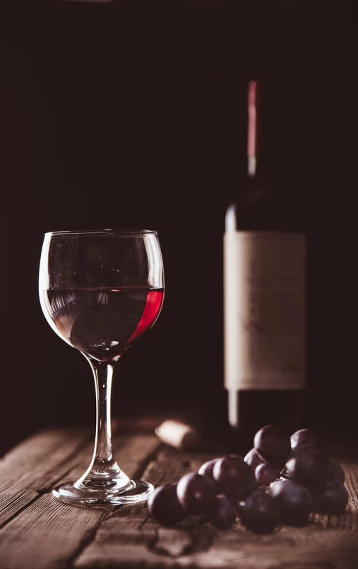 a glass of wine next to a bottle of wine, a still life, pexels, photorealism, barely lit warm violet red light, close-up product photo, stock photo, dark photo