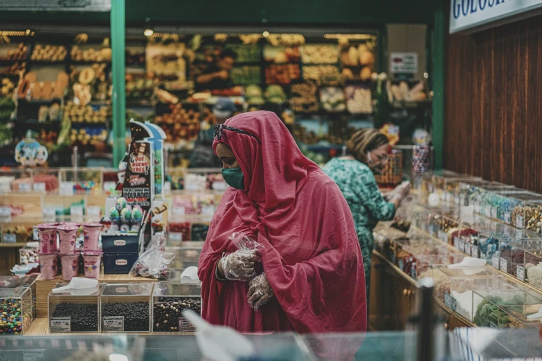 a woman in a red robe standing in a store, by Maryam Hashemi, pexels, hyperrealism, wearing facemask, fresh food market people, pink and green, an arab standing watching over