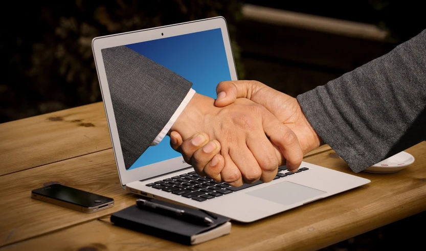 two people shaking hands in front of a laptop, a stock photo, by Matt Cavotta, shutterstock, renaissance, complexly detailed, photo realistic, high-tech devices, detailed zoom photo