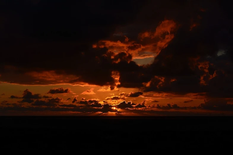 the sun is setting on the horizon of the ocean, a picture, by Tom Carapic, burning clouds, darkness dramatic, distant clouds, ; wide shot