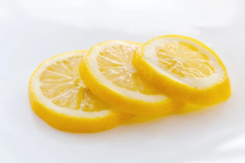 a white plate topped with slices of lemon, a picture, by Jan Kupecký, pexels, minimalism, glossy surface, with a white background, citrinitas, rule of three