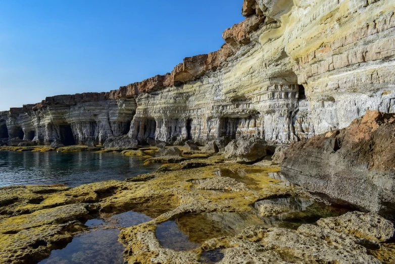 a rock outcropping next to a body of water, a picture, by Simon Marmion, shutterstock, les nabis, cyprus, layers of strata, stock photo, cave system