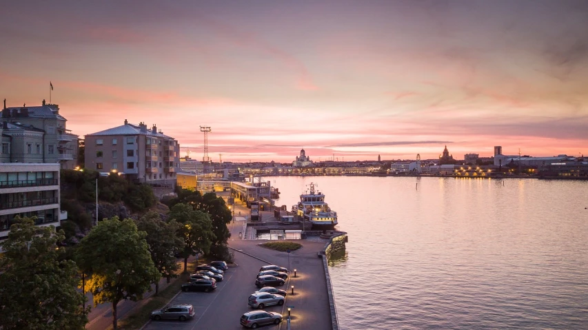 cars parked on the side of a road next to a body of water, by karlkka, shutterstock, vista of a city at sunset, helsinki, pink sunset, port
