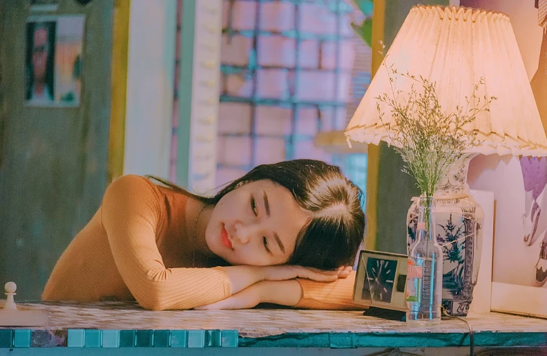 a woman laying on top of a table next to a lamp, a picture, inspired by Kim Jeong-hui, tumblr, jaeyeon nam, soft neon atmosphere, thoughtful pose, lofi portrait