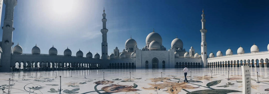 a man standing in front of a large white building, a colorized photo, by Tom Wänerstrand, pexels contest winner, with beautiful mosques, arabian princess, domes, realistic painting of a complex