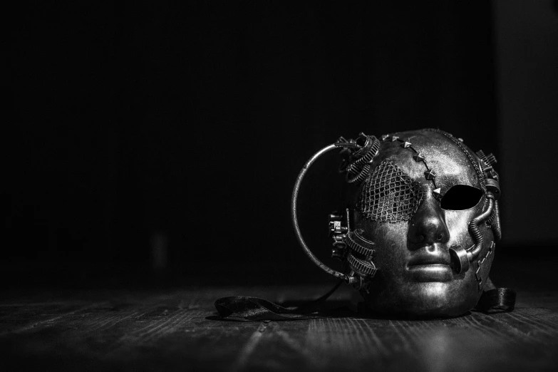 a metal mask sitting on top of a wooden floor, unsplash, surrealism, dark industrial atmosphere, eerie music, monochromatic photo, chainmail