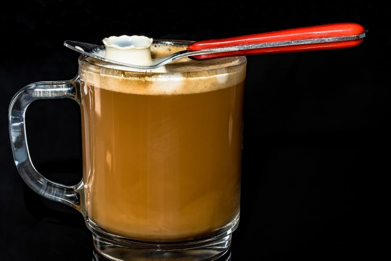 a cup of coffee with a spoon sticking out of it, by Thomas Häfner, inside a beer glass, with a black background, colored milk tea, butter