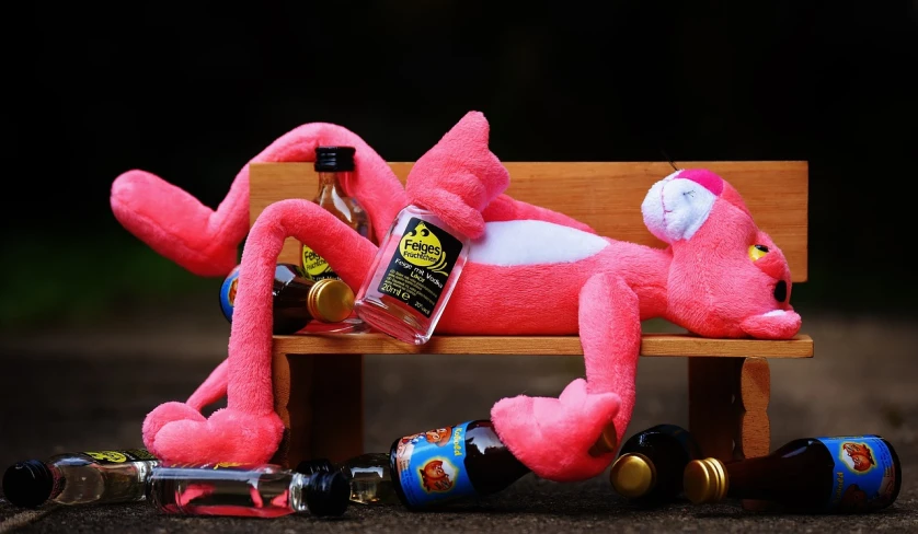 a pink stuffed animal laying on top of a wooden bench, a picture, by Doug Ohlson, alcohol, six arms, booze, ren and stimpy style