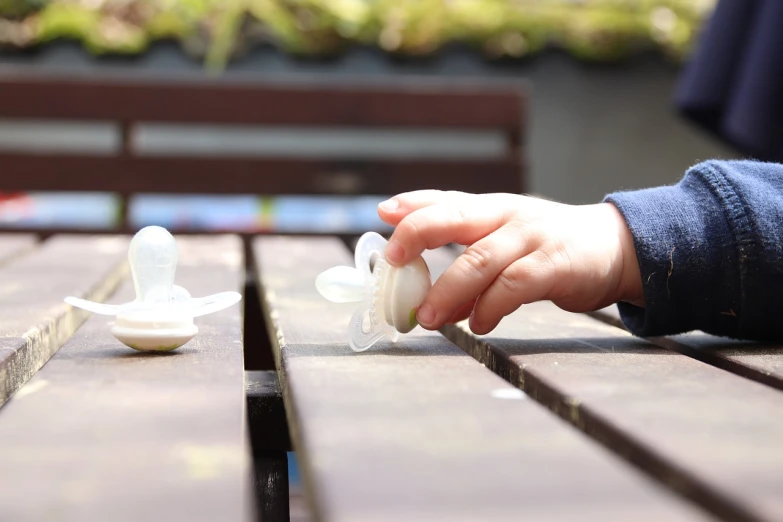 a close up of a person's hand on a wooden table, a picture, plastic toy, at the terrace, nipple, innocence