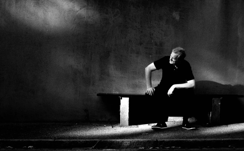 a black and white photo of a man sitting on a bench, by Leo Leuppi, minimalism, low key lights, grieving, grungy, tim rees