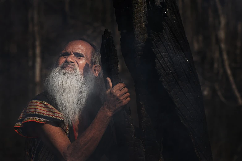 a man with a long white beard standing next to a tree, a portrait, by Sunil Das, pexels contest winner, sumatraism, ancient blacksmith god, incense smoke fills the air, alligator shaman, mana shooting from his hands