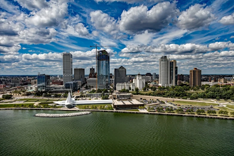 a large body of water with a city in the background, by Andrew Domachowski, flickr, renaissance, wisconsin, capital plaza, tyndall rays, partly cloudy day