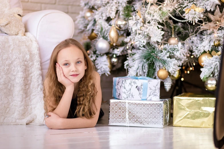 a little girl laying on the floor in front of a christmas tree, a portrait, by Maksimilijan Vanka, pixabay, realism, photoshoot for skincare brand, birthday wrapped presents, 😭🤮 💔, a beautiful teen-aged girl