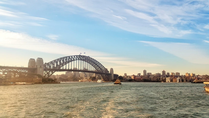 a large body of water with a bridge in the background, a picture, inspired by Sydney Carline, pexels, harbour in background, 1128x191 resolution, the photo was taken from a boat, brown