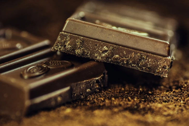 a couple of pieces of chocolate sitting on top of a table, a picture, pexels, happening, black gold, rectangular, dark brown, eating