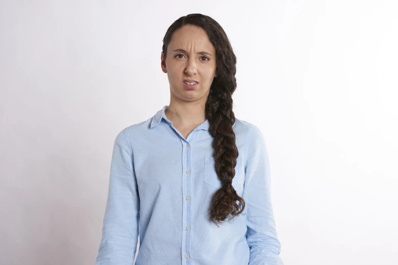 a woman standing in front of a white wall, a portrait, antipodeans, annoyed facial expression, two long braids blue, man esthete with disgust face, mixed race