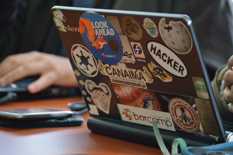 a person sitting at a desk with a laptop covered in stickers, by Tom Carapic, flickr, csgo sticker, camp, hackerman, up close image