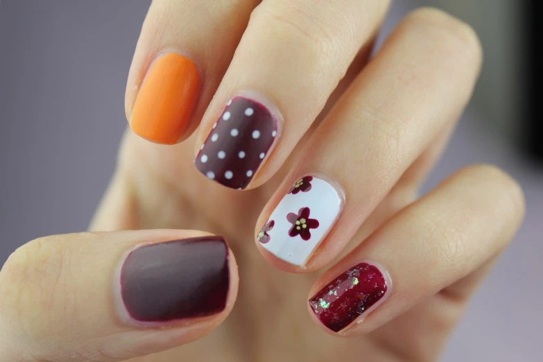 a close up of a person's hand with a colorful manicure, brown flowers, polkadots, maroon and white, gray and orange colours