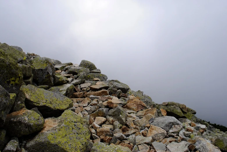 a pile of rocks sitting on top of a mountain, a picture, by Aleksander Gierymski, flickr, overcast!!!, walking to the right, lichen, traverse