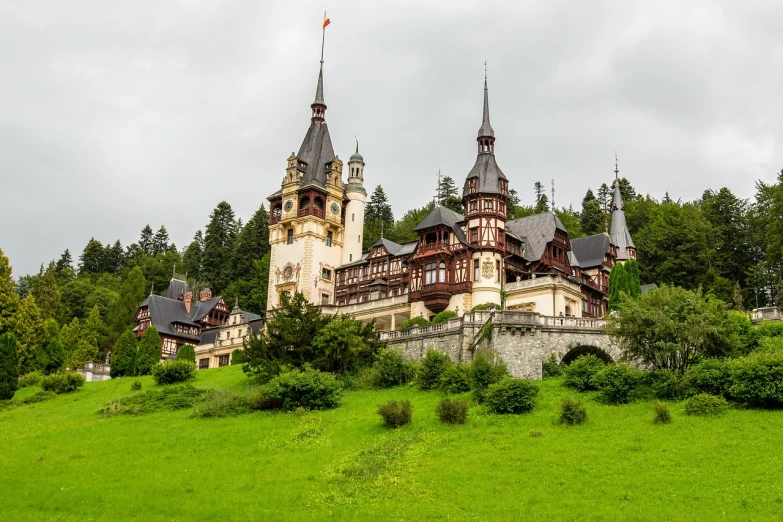 a castle sitting on top of a lush green hillside, a photo, shutterstock, art nouveau, wooden buildings, romanian, on a cloudy day, highly ornate intricate details