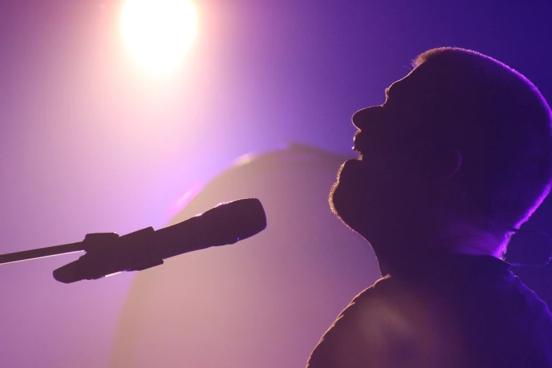 a man that is standing in front of a microphone, a picture, by Tom Carapic, pexels, back lit, colin hay, show from below, purple light