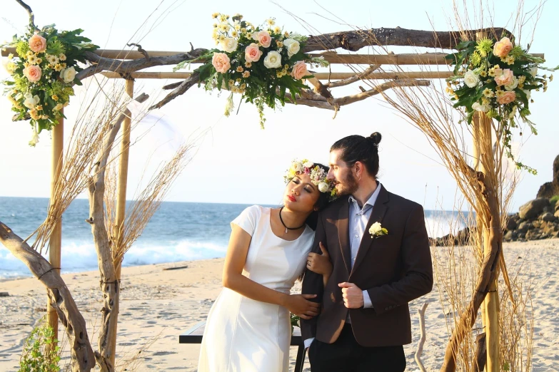 a man and woman standing next to each other on a beach, a portrait, by Juan O'Gorman, pexels, romanticism, floral headpiece, an archway, rustic, celebrating an illegal marriage