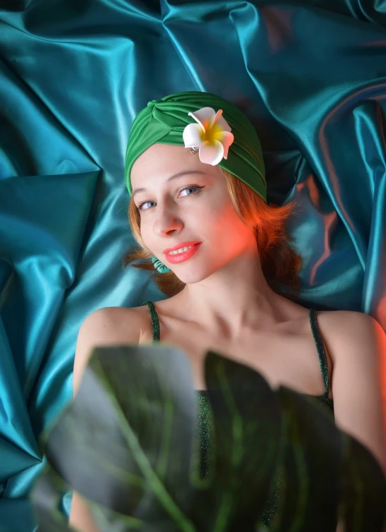 a woman laying on a bed with a flower in her hair, a portrait, inspired by Konstantin Somov, art deco, fashion color studio lighting, green swimsuit, turban of vibrant flowers, beauty woman in holograms