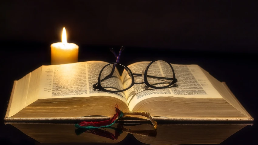 an open book sitting on top of a table next to a candle, reading glasses, biblical art lighting, praying, spectacled