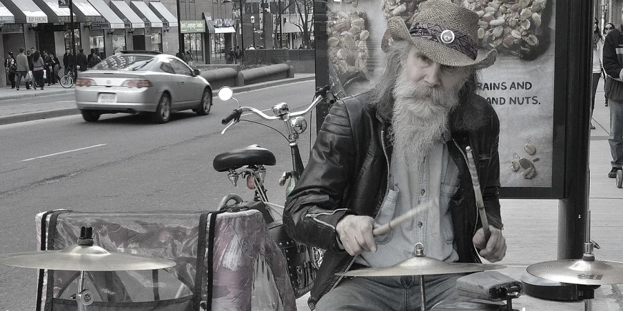 a man with a long beard playing drums, a photo, inspired by Bruce Gilden, flickr, photorealism, desaturated!, some people around ”, toronto, motorcycles