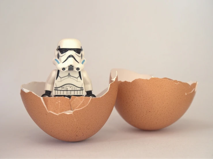 a toy stormtrooper is sitting in an egg shell, a picture, inspired by George Lucas, reduce duplicate content, 6 4 0, hero shot, grain”