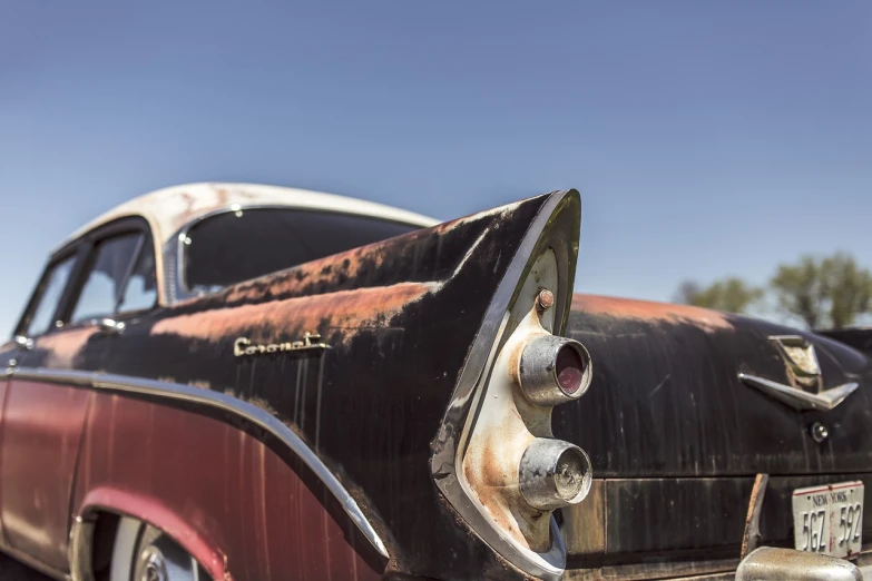 an old black and red car parked in a parking lot, by Peter Churcher, unsplash, photorealism, rust and corrosion, tail fin, 1957 chevrolet bel air, detail shot