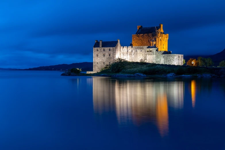 a castle sitting on top of a hill next to a body of water, a picture, by Andrew Robertson, blue hour lighting, scott roberston, reflections on the water, bright blue glowing water