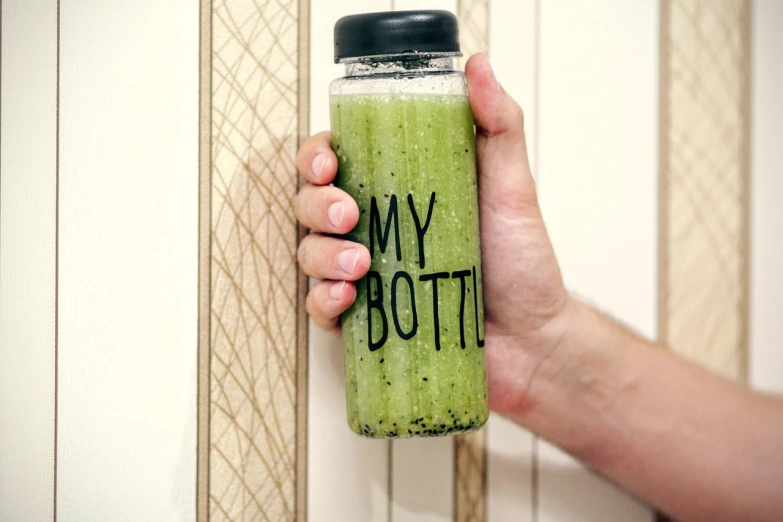 a person holding a bottle of green smoothie, a picture, by Ramón Silva, diy, lettering clean, glass jar, bored